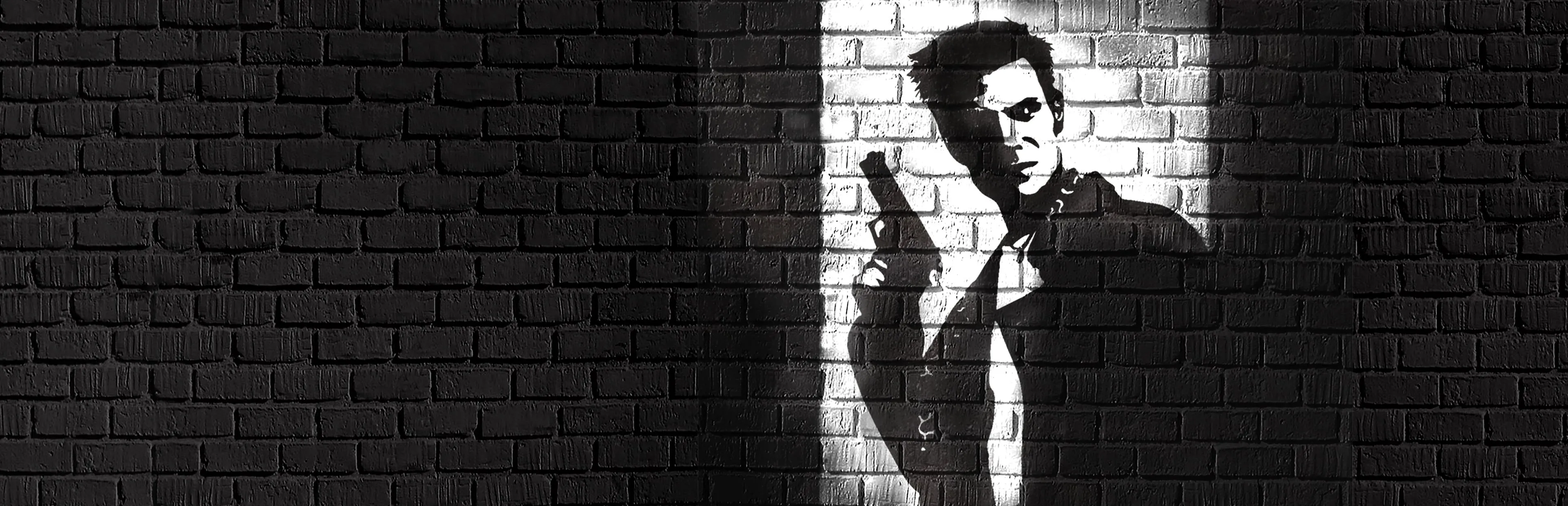 Max Payne — key art: Max’s stencil silhouette with a pistol on a brick wall, in a single pool of light